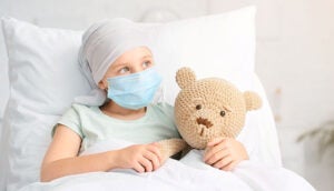 Child in a hospital bed with a mask holding a teddy bear.